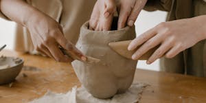 Hands shaping clay pottery collaboratively, showing craftsmanship.