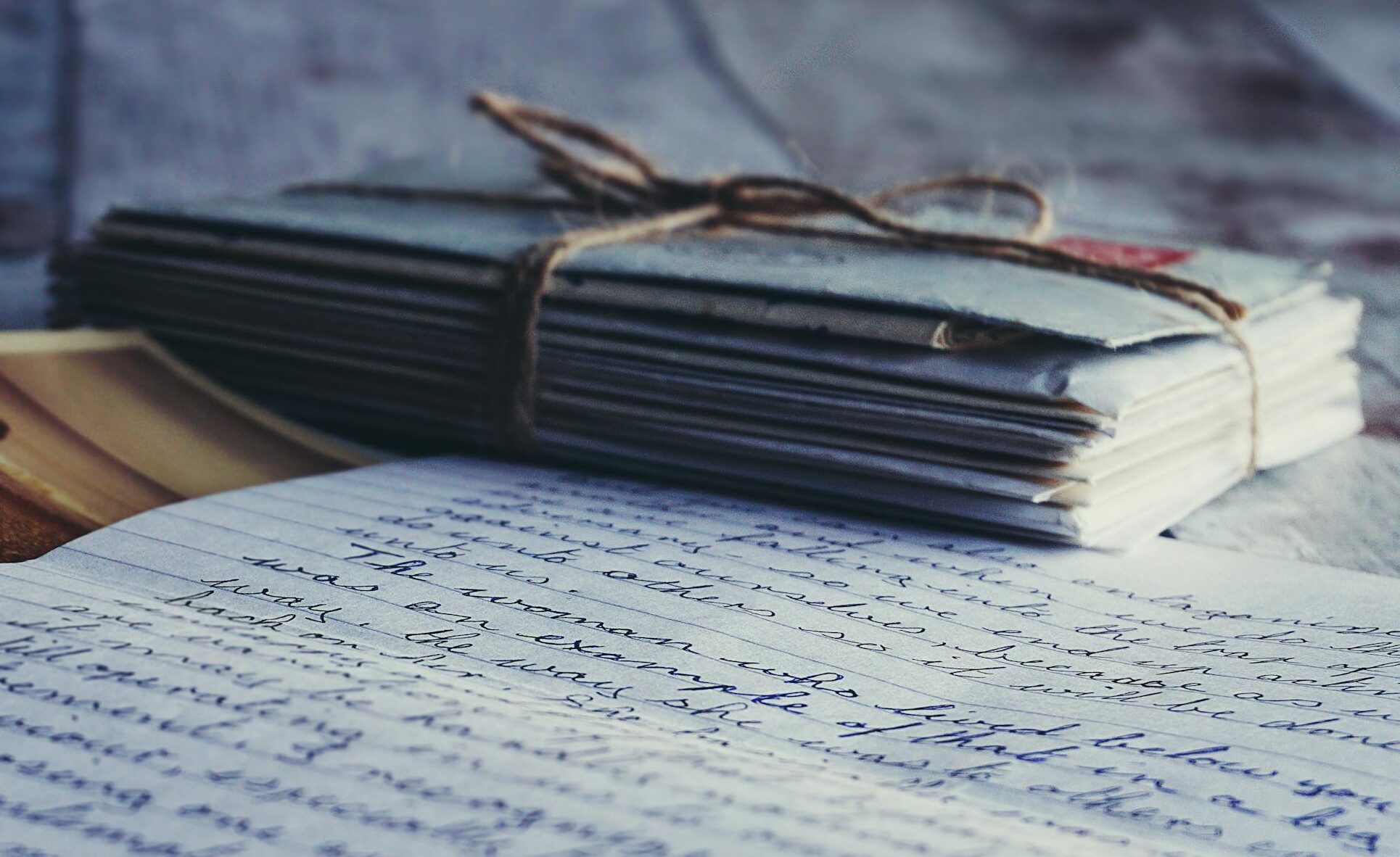Stack of vintage letters and photographs tied with string on a rustic wooden table.