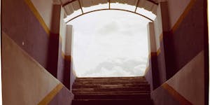 Architectural stairs leading to a bright, cloudy sky, framed by colorful walls.