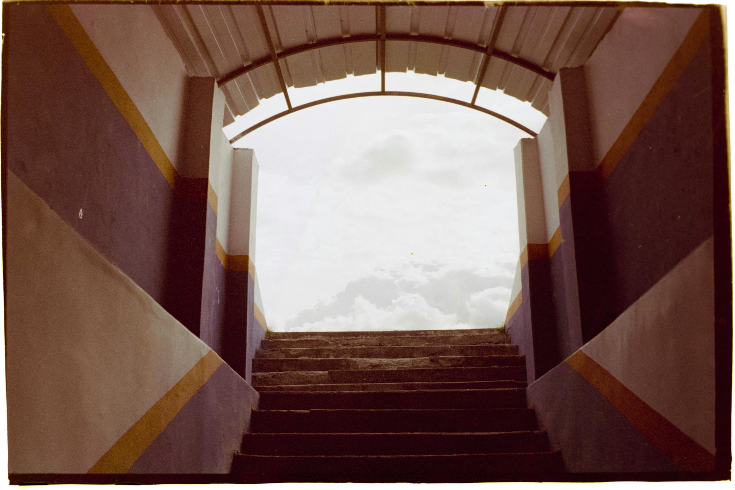 Architectural stairs leading to a bright, cloudy sky, framed by colorful walls.